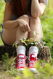 Woman sitting on stump with flowers in socks outdoors, closeup