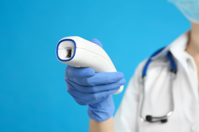 Doctor holding non contact infrared thermometer against light blue background, focus on hand. Measuring temperature