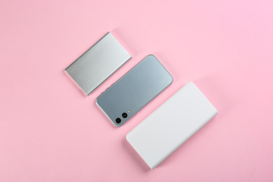 Mobile phone and portable chargers on pink background, flat lay