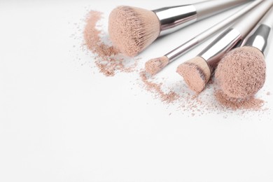 Photo of Different makeup brushes with crushed cosmetic product on light background, closeup. Space for text