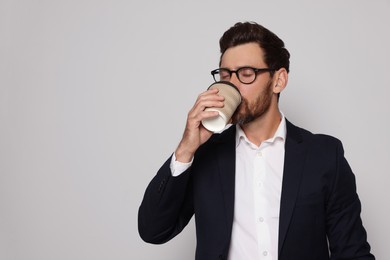 Handsome bearded man with glasses drinking from paper cup on light grey background. Space for text
