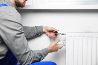 Professional plumber using pliers while preparing heating radiator for winter season, closeup