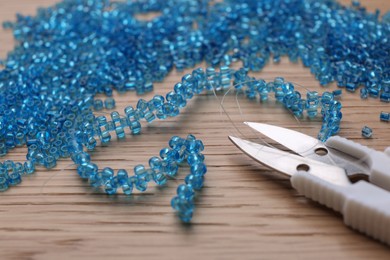 Bright light blue glass beads, bracelet and scissors on wooden table, closeup