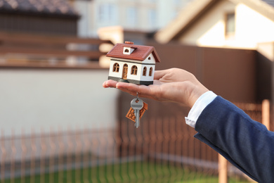 Real estate agent holding key and house model outdoors, closeup