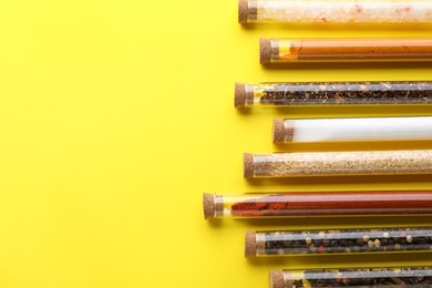 Glass tubes with different spices on yellow background, flat lay. Space for text