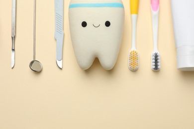 Tooth model with cute face, oral care products and dental tools on beige background, flat lay. Space for text
