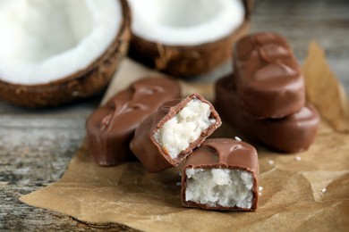 Delicious milk chocolate candy bars with coconut filling on wooden table, closeup