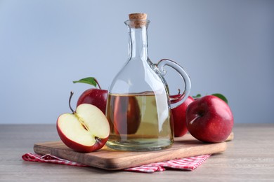 Jug of tasty juice and fresh ripe red apples on wooden table