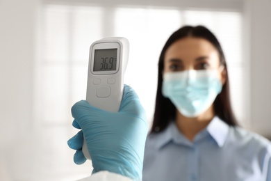 Doctor measuring woman's temperature in office, closeup. Prevent spreading of Covid-19