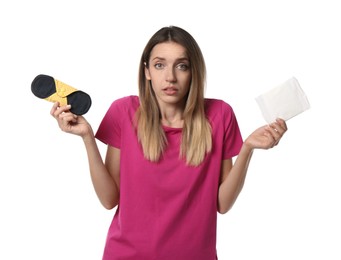 Confused young woman with disposable and reusable cloth menstrual pads on white background