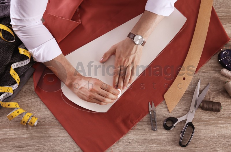 Photo of Tailor working with cloth at table in atelier, top view