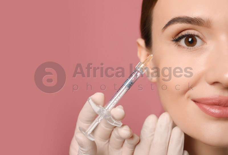 Beautiful woman getting facial injection on pink background, closeup. Cosmetic surgery