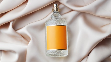 Photo of Luxury bottle of perfume on beige silk, top view