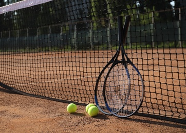 Tennis balls and rackets near net on clay court