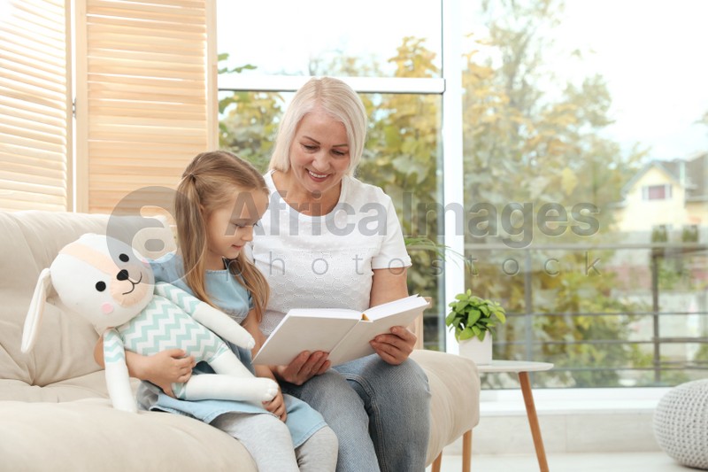 Happy grandmother with her granddaughter reading book together at home