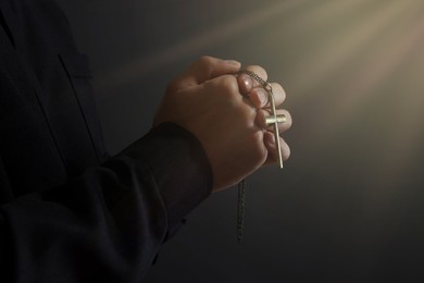 Holy light and priest with cross praying on black background, closeup