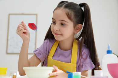 Cute little girl mixing ingredients with silicone spatula at table in room. DIY slime toy