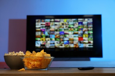 Bowls of snacks and TV remote control on table indoors
