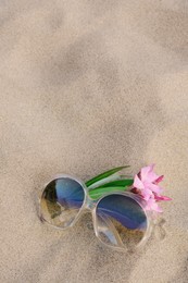 Photo of Beautiful sunglasses with tropical flower on sandy beach, space for text