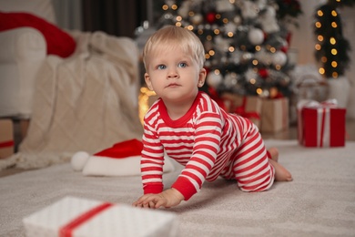 Cute baby in Christmas pajamas crawling on floor at home