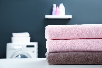 Photo of Stack of clean towels on table in laundry room, closeup. Space for text
