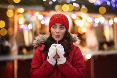 Happy young woman with cup of drink on city street in evening. Christmas celebration