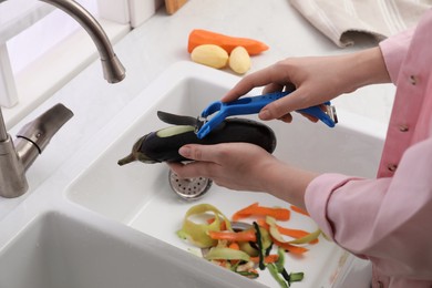 Woman peeling cucumber over kitchen sink with garbage disposal at home, closeup
