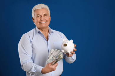 Happy senior man with cash money and piggybank on blue background