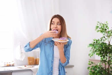 Photo of Beautiful young woman eating donut in kitchen. Failed diet