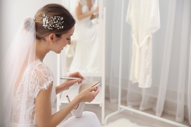 Young bride writing on her shoe indoors, space for text. Wedding superstition