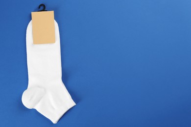 Pair of white cotton socks on blue background, top view. Space for text