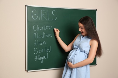 Pregnant woman writing different baby names on green chalkboard