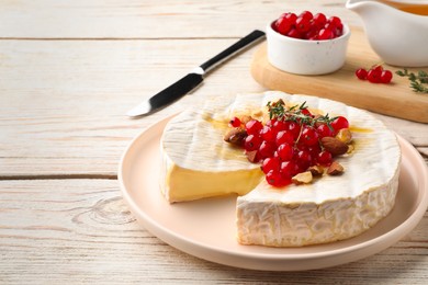 Brie cheese served with almonds, red currants and honey on white wooden table. Space for text