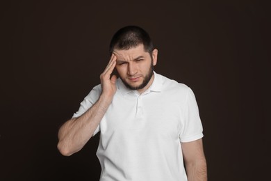 Man suffering from headache on dark brown background