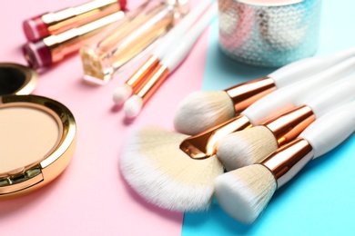 Professional makeup brushes and different decorative cosmetics on color background