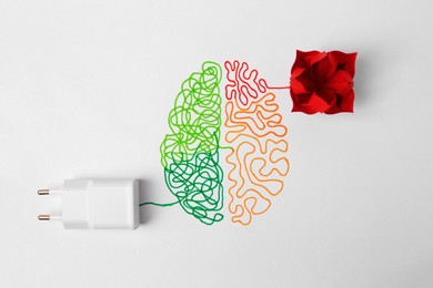 Photo of Drawn brain with charging adapter and red paper flower as solution idea on white background, flat lay