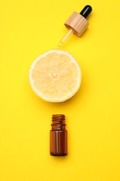 Bottle of citrus essential oil and fresh lemon on yellow background, flat lay