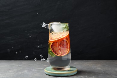 Delicious refreshing drink with sicilian orange splashing out of glass on grey table against black background