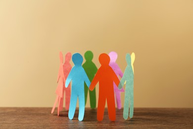 Photo of Many different paper human figures standing in circle on wooden table against beige background. Diversity and inclusion concept