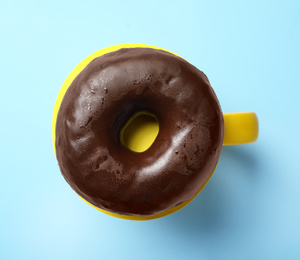 Cup of coffee made with donut on light blue background, top view