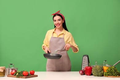 Photo of Young housewife with vegetables and different utensils on green background