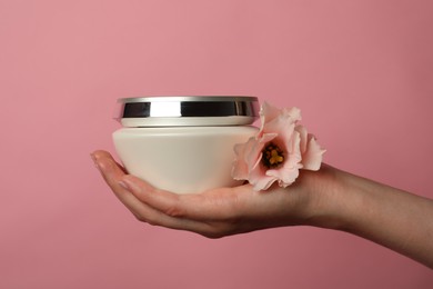 Photo of Woman holding jar of hair care cosmetic product and flower on pink background, closeup