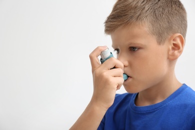 Photo of Little boy using asthma inhaler on light background