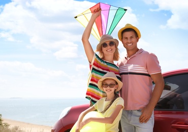 Happy family with inflatable ring and kite near car at beach