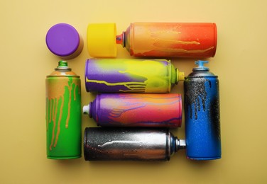Used cans of spray paints on beige background, flat lay. Graffiti supplies