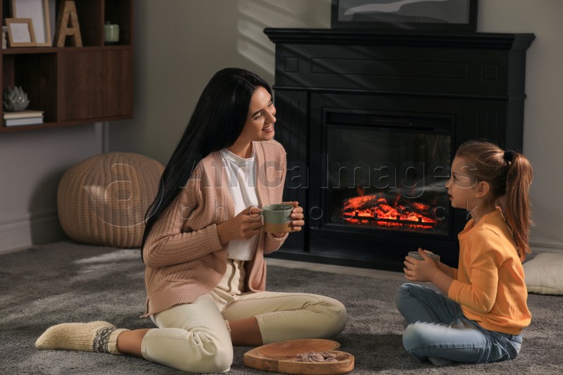 Happy mother and daughter spending time together on floor near fireplace at home