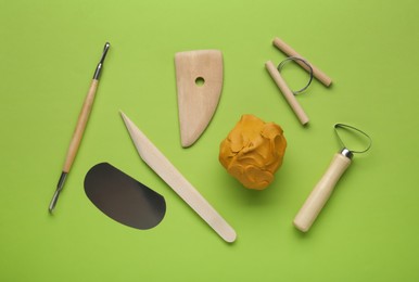 Photo of Clay and set of modeling tools on green background, flat lay