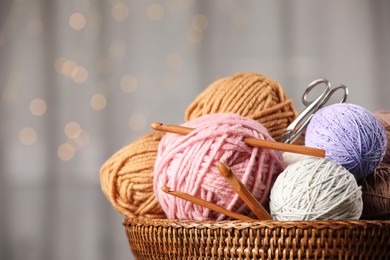 Photo of Wicker basket with clews of colorful knitting threads, crochet hooks and scissors indoors, closeup. Bokeh effect