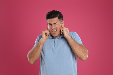 Emotional man covering ears with fingers on pink background