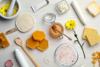 Flat lay composition with beeswax and cosmetic products on white wooden table